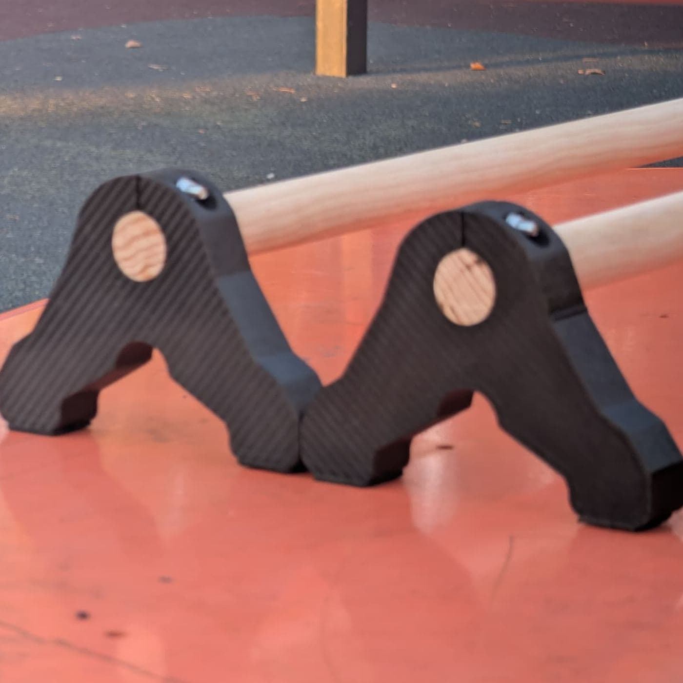 Dos soportes negros impresos en 3D junto a sus barras de madera sobre una superficie naranja