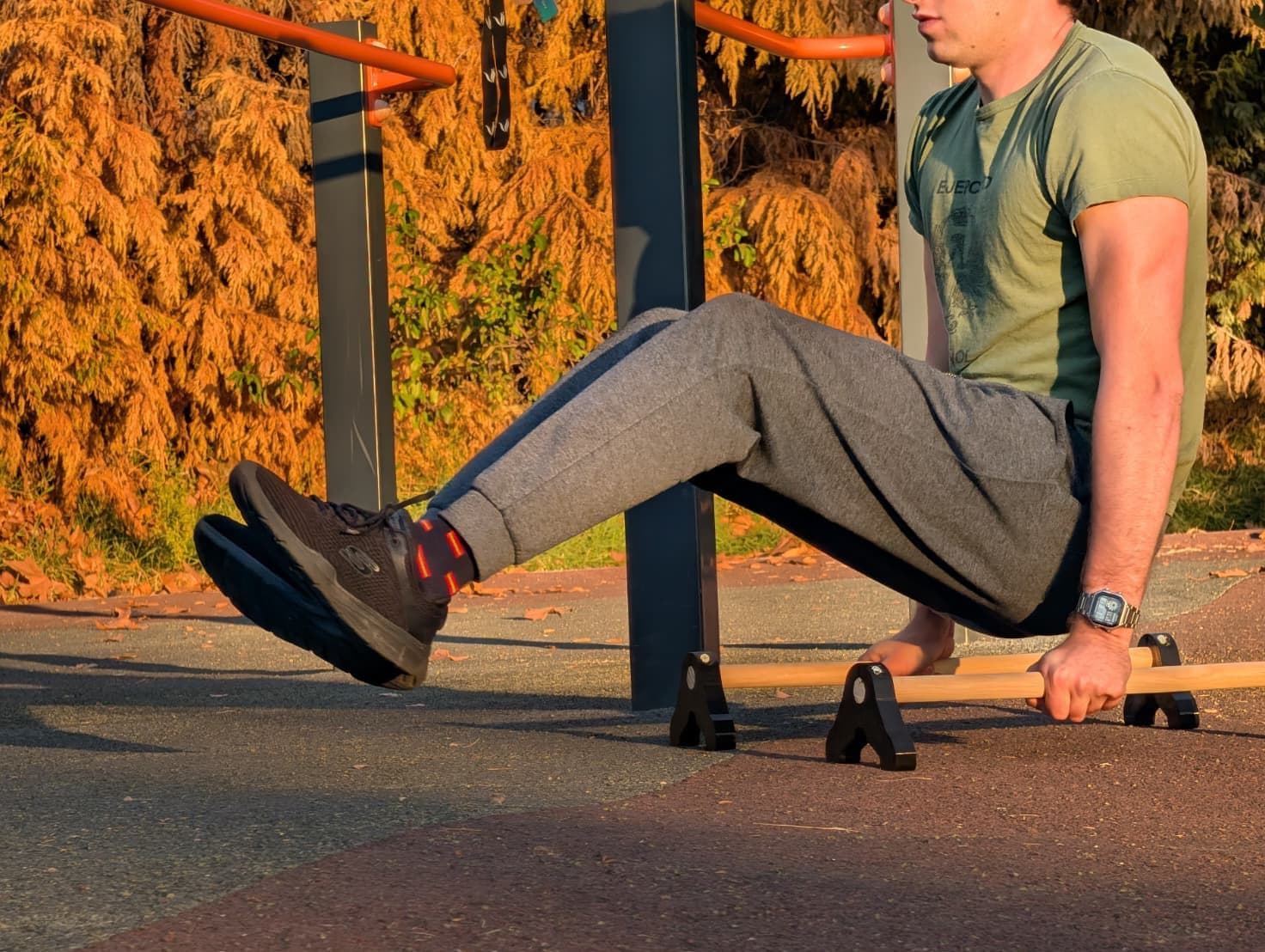 L-sit con piernas estiradas sobre unas paralelas de madera en un parque